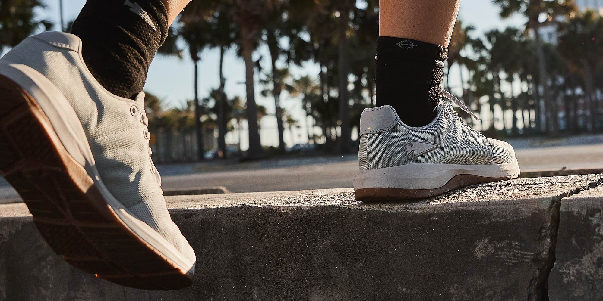 Person wearing white sneakers stepping onto a concrete platform, with palm trees in the background.