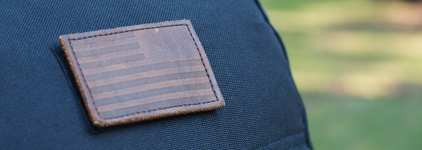 Close-up of a leather patch with an embossed American flag on a dark fabric background.