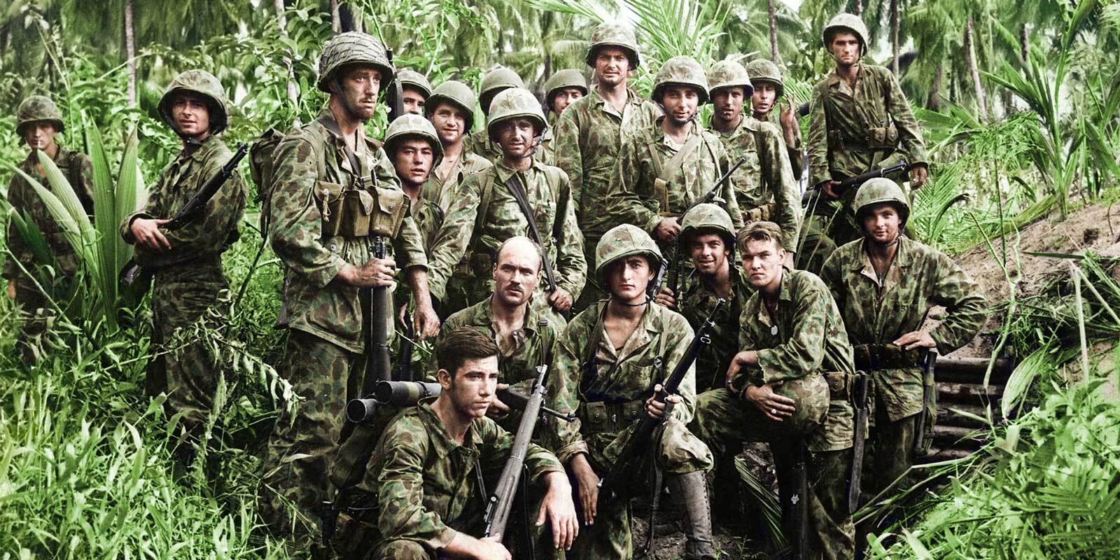 A group of soldiers in combat uniforms pose in a jungle setting.