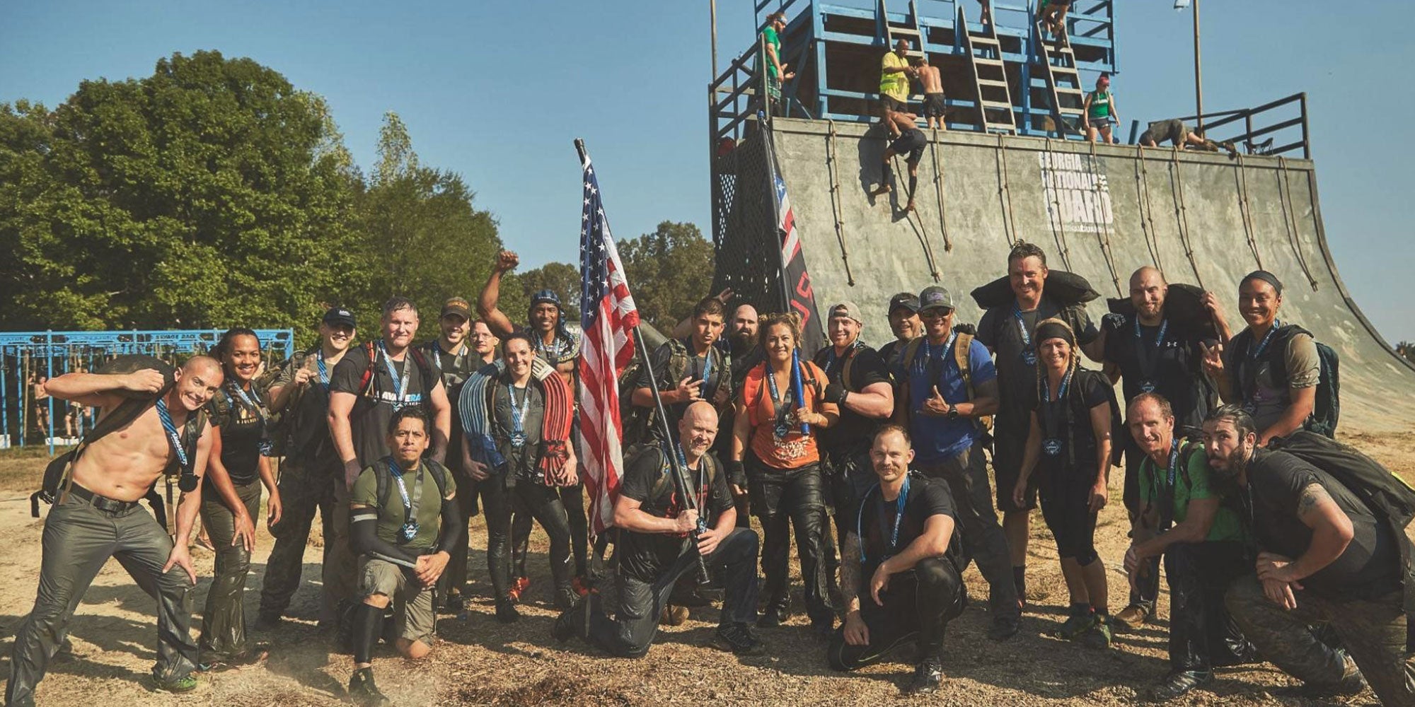 A group of people in athletic gear poses in front of a large ramp, holding flags, outdoors.