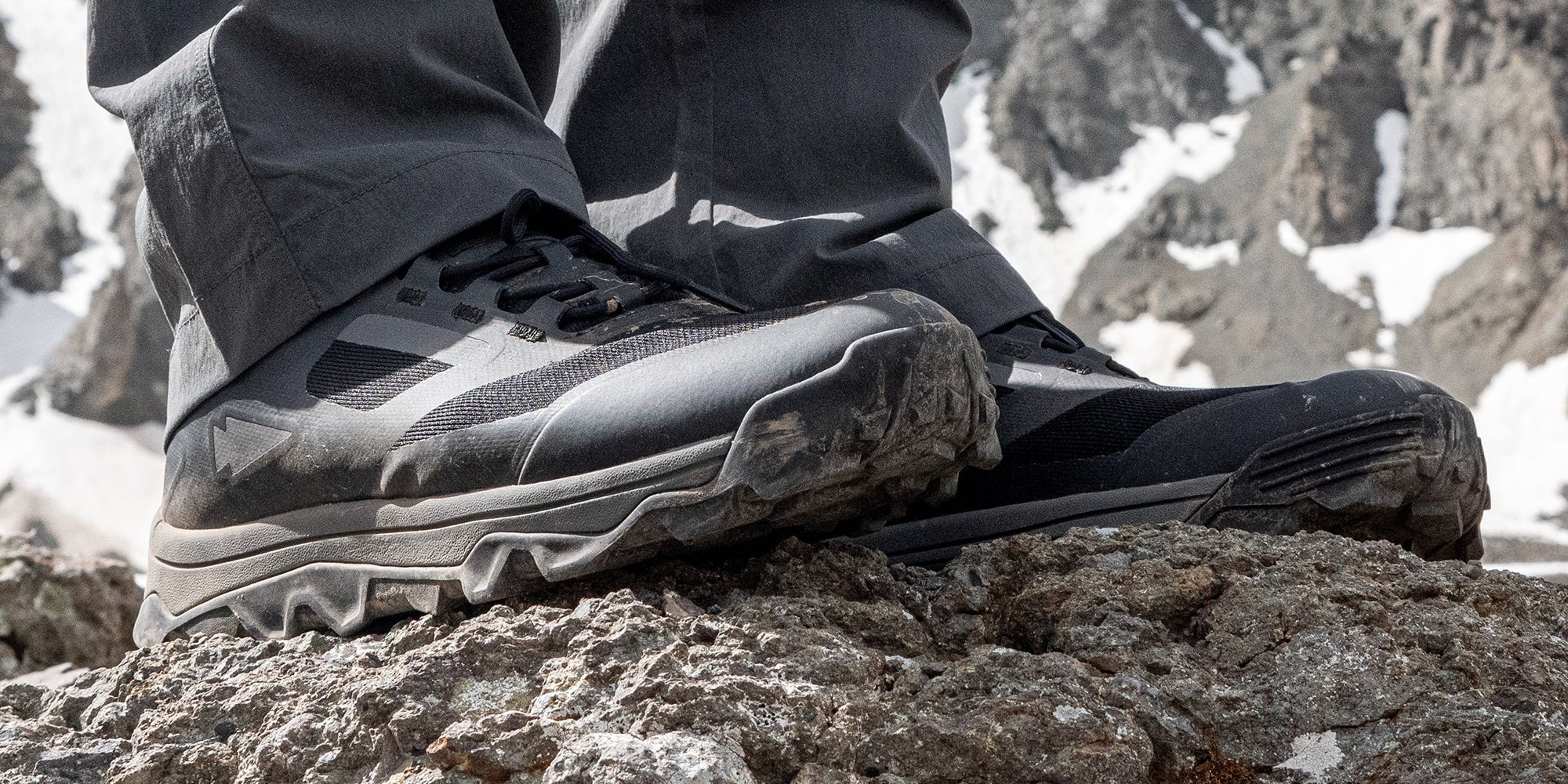 Close-up of hiking boots on rocky terrain with a mountainous background.