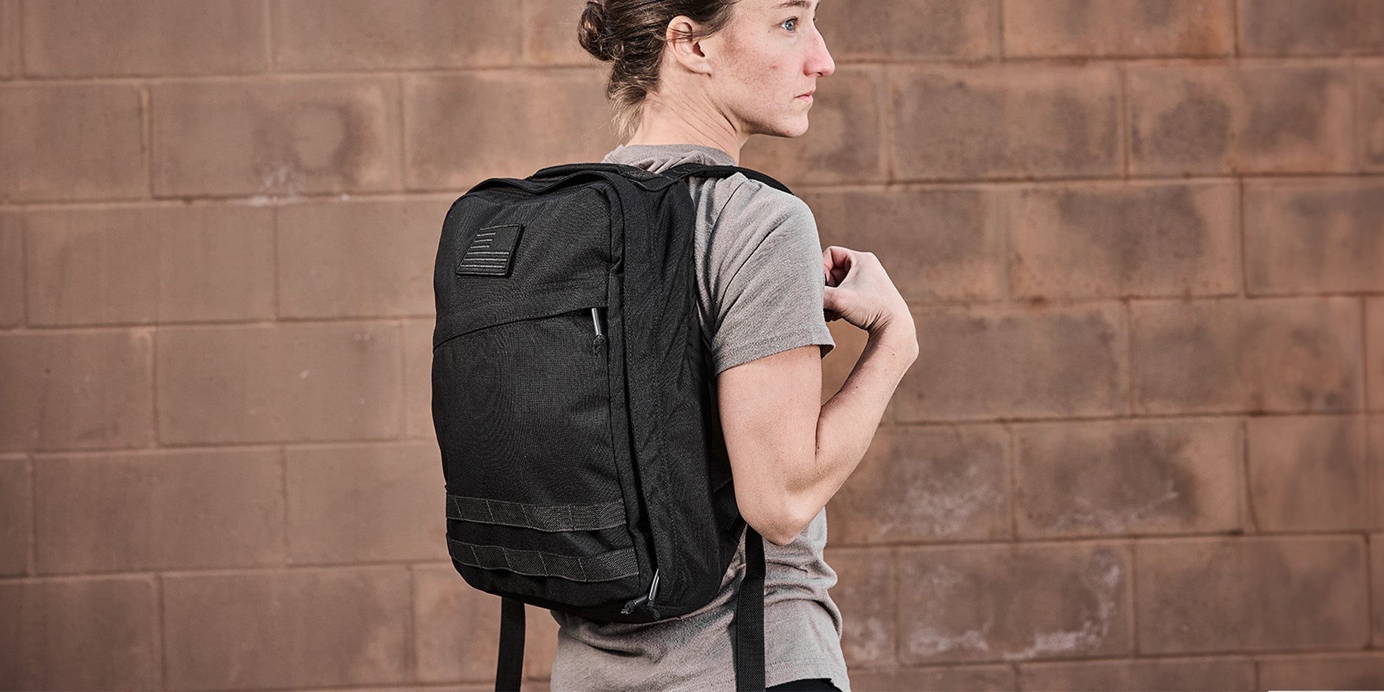 Person wearing a black backpack, standing against a textured brick wall.