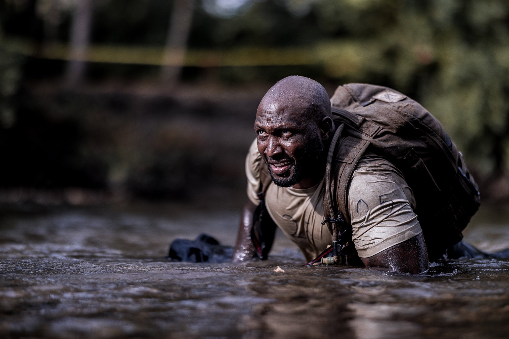 Person crawling through muddy water with a backpack in an outdoor setting.