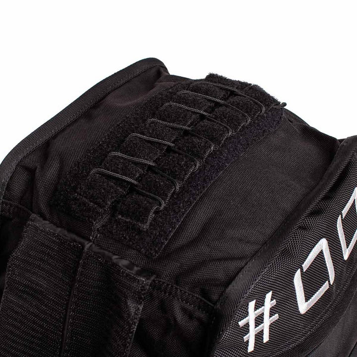 Close-up of the GORUCK Sand Tombstones, a black duffel bag with a velcro strap and stitched loops on the side, ideal for loaded carries. Its textured fabric showcases a partially visible white embroidered hashtag with numbers, adding an element of intrigue to the design.