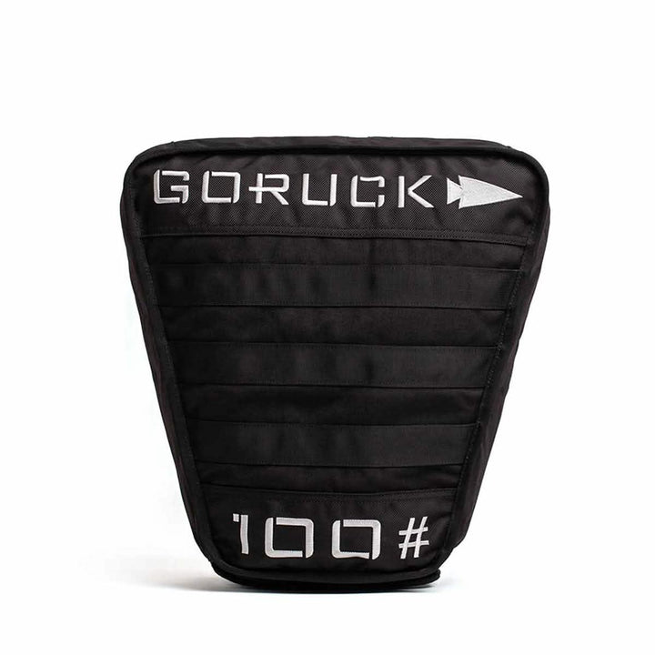 The Sand Tombstones by GORUCK is a black sandbag adorned with white text and an arrow logo, featuring "100" at the bottom. Designed in the style of a Husafell Sandbag, it offers a structured rectangular shape with horizontal stitching and a multilayer closure system perfect for loaded carries.