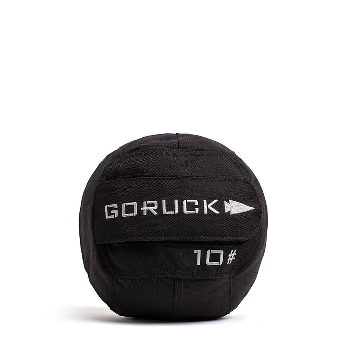 A GORUCK Sand Medicine Ball in black, featuring "10#" printed in white text, is perfect for core stability. It comes with fabric straps for easy handling, making it a great addition to your home gym.