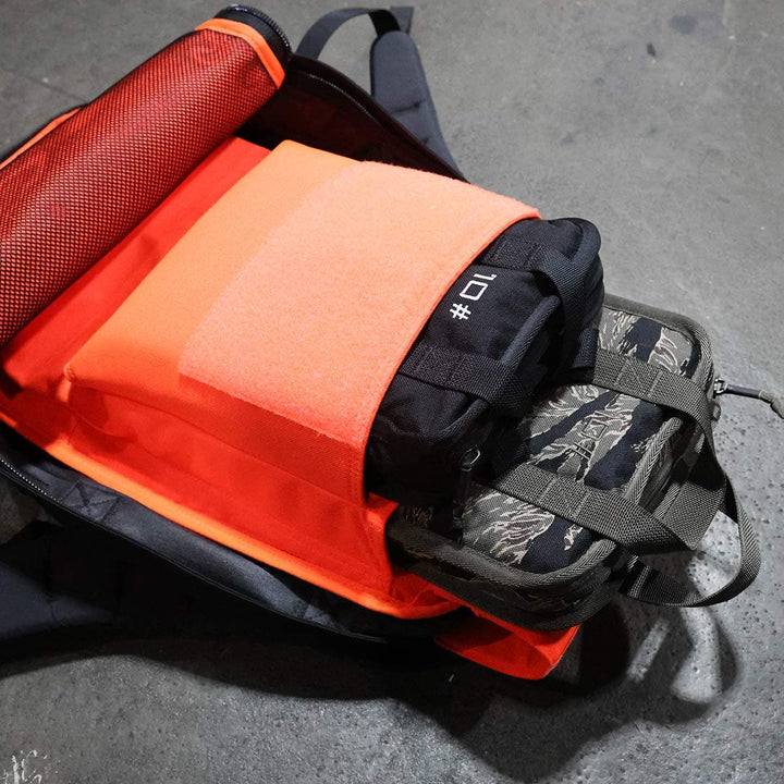 Open backpack displaying neatly packed electronic devices and accessories, ready for rucking adventures. A portable **Sand Ruck Plate** from **GORUCK** is nestled among the gear, ensuring you’re prepared and balanced for every step of your journey.