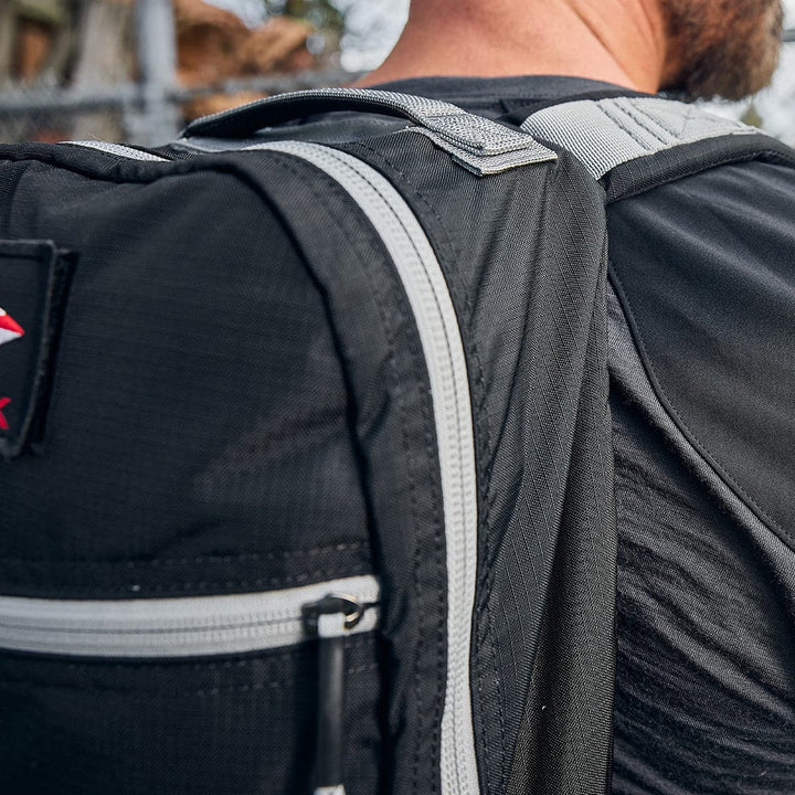 Close-up of a person outdoors wearing the GORUCK Bullet Ruck Laptop backpack, made from ripstop nylon in black with a gray zipper, boasting a water-resistant design and lumbar support for ultimate comfort.