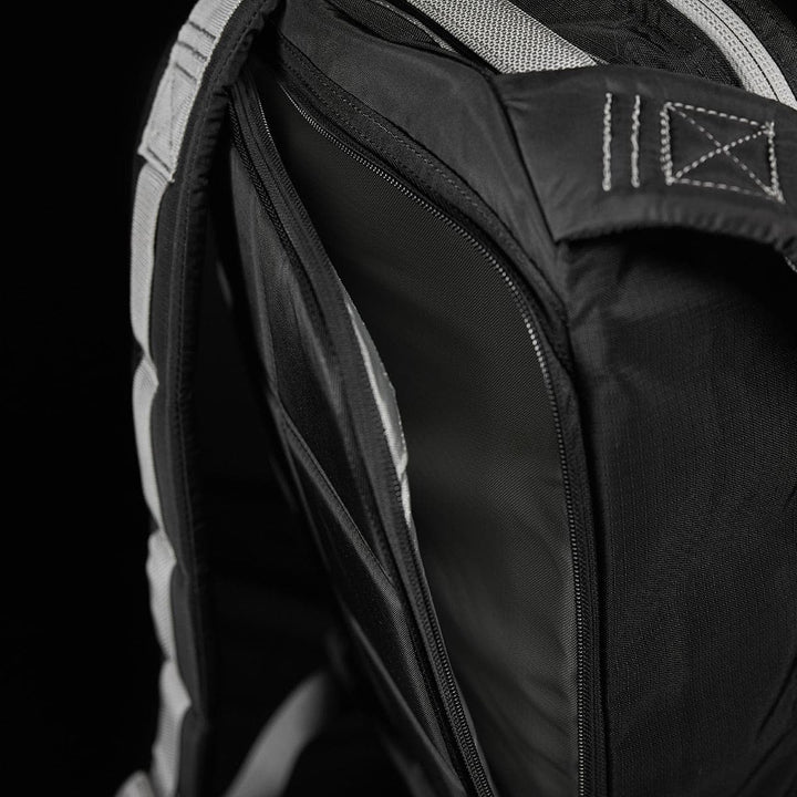 A close-up of the Bullet Ruck Laptop - Ripstop Nylon - 16L by GORUCK showcases its black design with a partially open zipper, revealing the water-resistant interior and dedicated laptop compartment, set against a dark background.