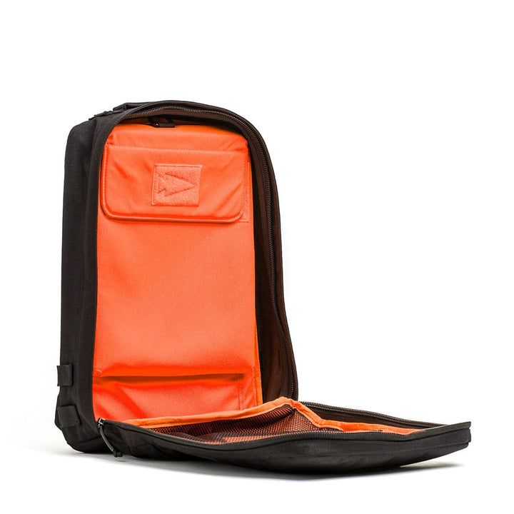 The GORUCK Rucker 4.0 backpack in black boasts a vibrant orange interior, displayed open with a visible zipper pocket.