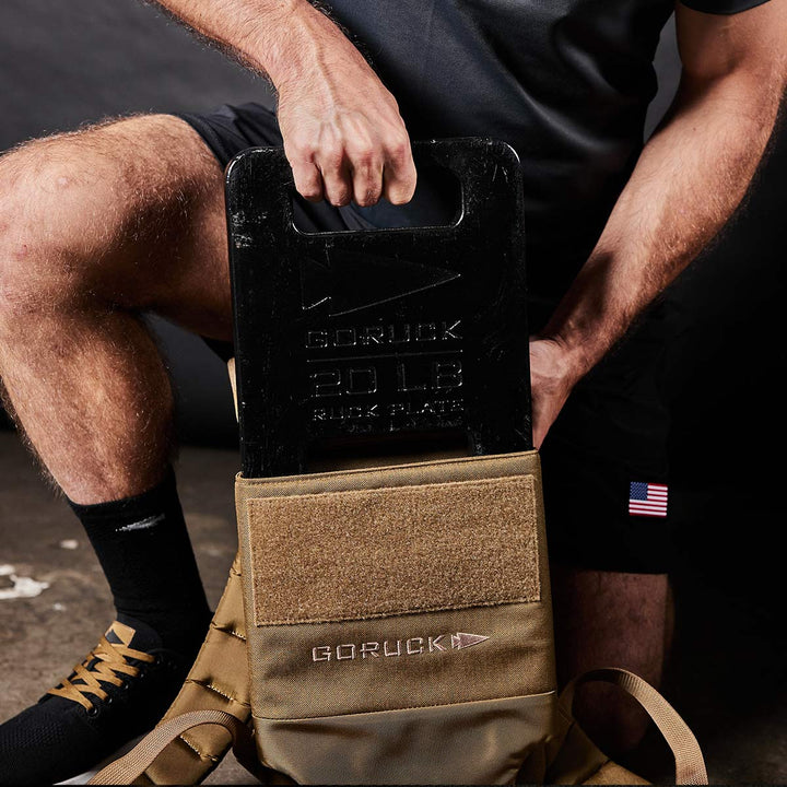 A dedicated rucker steadily lifts a GORUCK Ruck Plate - 20 lb, sliding it effortlessly into the tactical backpack designed for optimal performance and comfort.