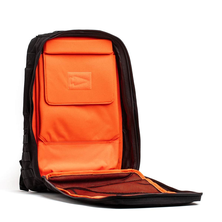 The GORUCK Rucker 4.0, shown standing upright against a white background, is an open black rucksack with a vibrant orange interior. It features multiple compartments, including a padded laptop sleeve and a mesh pocket, making it perfect for rucking adventures.