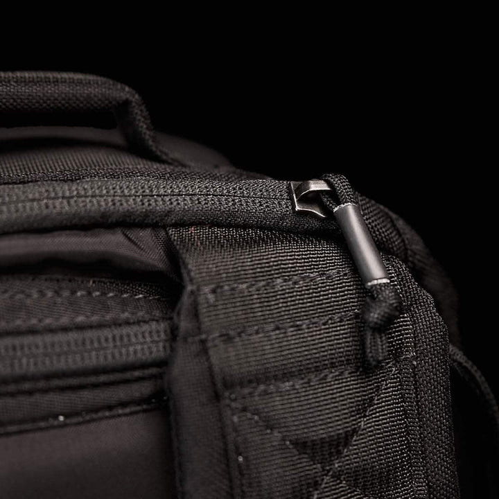 Close-up of a black fabric bag's zipper and strap against a black background, highlighting the durability of GORUCK's GR1 USA, made with 210D CORDURA material commonly used in rugged rucksacks.