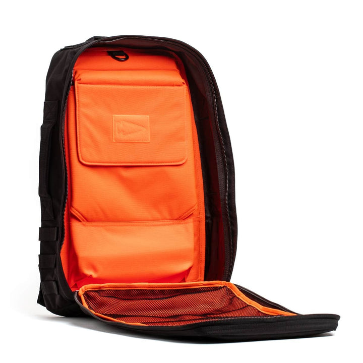 A GORUCK Rucker 4.0 backpack in black is open, showcasing its vibrant orange interior. The inside includes multiple compartments, such as a spacious padded section and a mesh pocket on the flap, ideal for organizing rucking essentials.