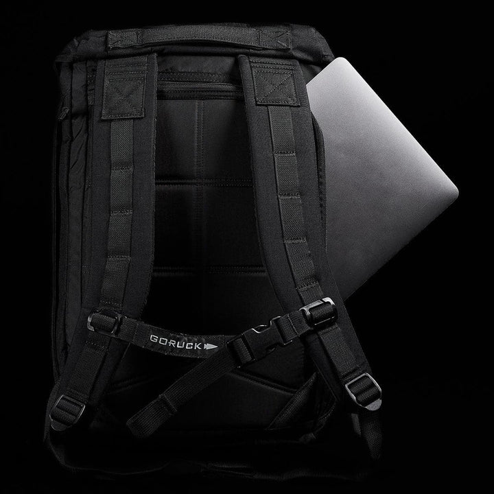 A stylish rucksack crafted from durable Cordura material, the M23 by GORUCK features robust straps and includes a compartment designed for a partially inserted laptop. This black backpack stands out distinctively against a plain black background.