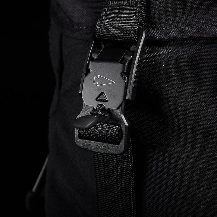 Close-up of a GORUCK M23 - Cordura backpack strap with a plastic buckle featuring an arrow design. Crafted from durable materials, this modern rucksack component stands out against the black background, highlighting the texture and details of the strap and buckle.