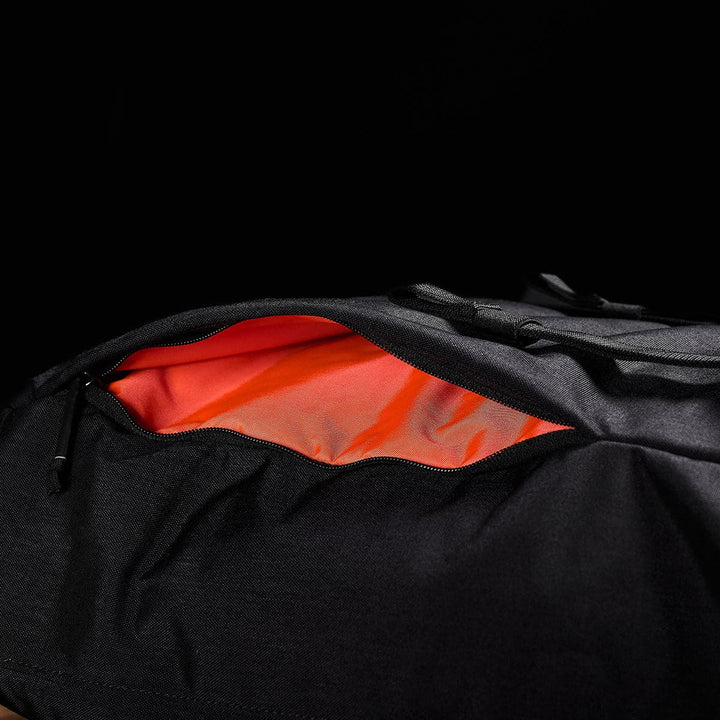 An M23 - Cordura rucksack by GORUCK, partially unzipped to reveal a bright orange interior lining against a dark background, showcasing its modern design and durable materials.