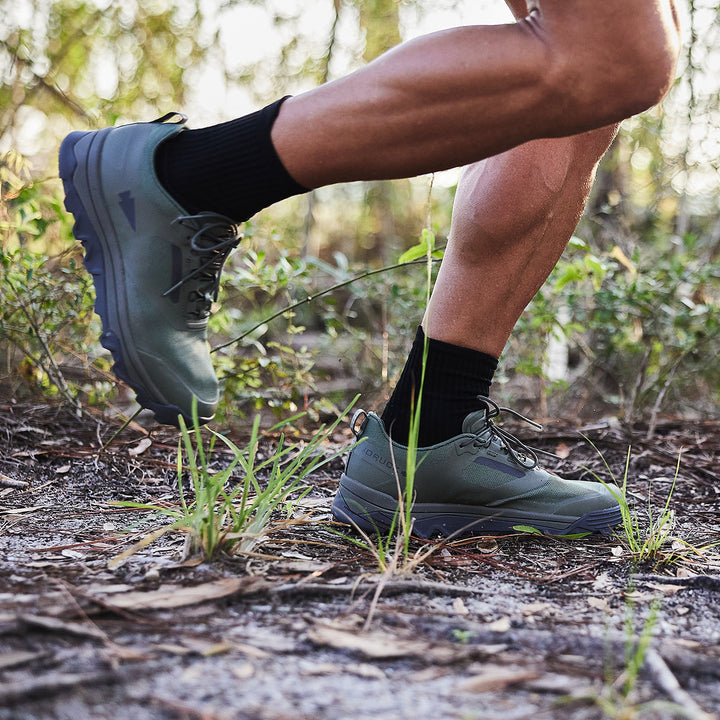 A person jogging on a forest trail, wearing Mackall - Earth + Forged Iron shoes from GORUCK and black socks, showcases the endurance suited for Special Forces training.