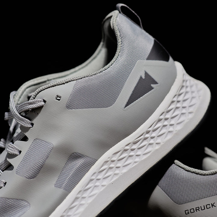 Close-up of the GORUCK Rough Runner - Speed Grey + White ultra-supportive running shoes, showcasing a textured white sole with a versatile road-to-trail outsole, set against a sleek black background.