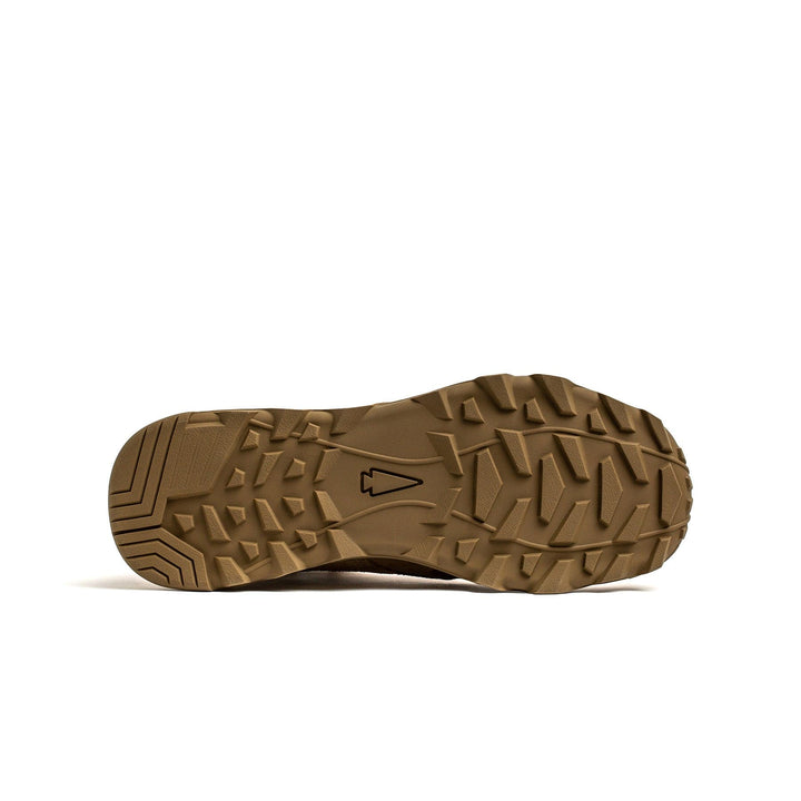 The image showcases the underside of a tan shoe sole from the GORUCK MACV-2 - Mid Top - Coyote, featuring deep, angular treads and a central arrow symbol. With its triple compound outsole, this design provides exceptional traction and durability, making it perfect for navigating rugged terrains like a jungle boot.