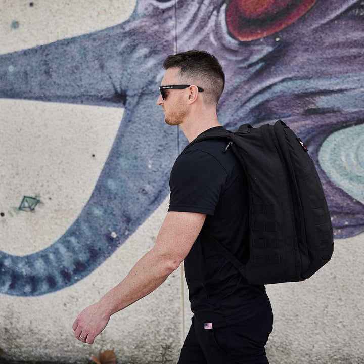 A person in black, sporting a GORUCK GR2 - USA backpack made from 210D CORDURA®, walks past a colorful wall mural.