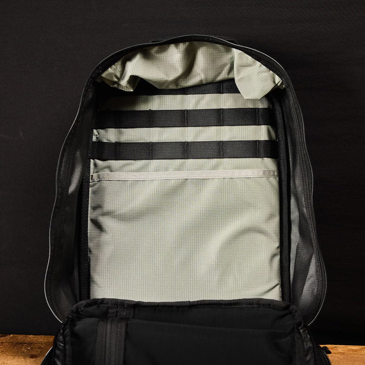 Open the GORUCK Bullet Ruck Double Compartment in black with a grey interior and dual compartments, featuring multiple elastic straps, set against a dark background.