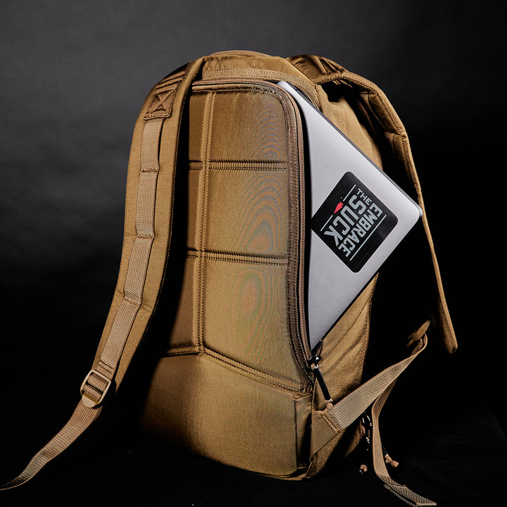 The GORUCK Bullet Ruck Laptop - 16L features a brown backpack with a bombproof laptop compartment, shown half-zipped with a laptop inside, set against a dark background.