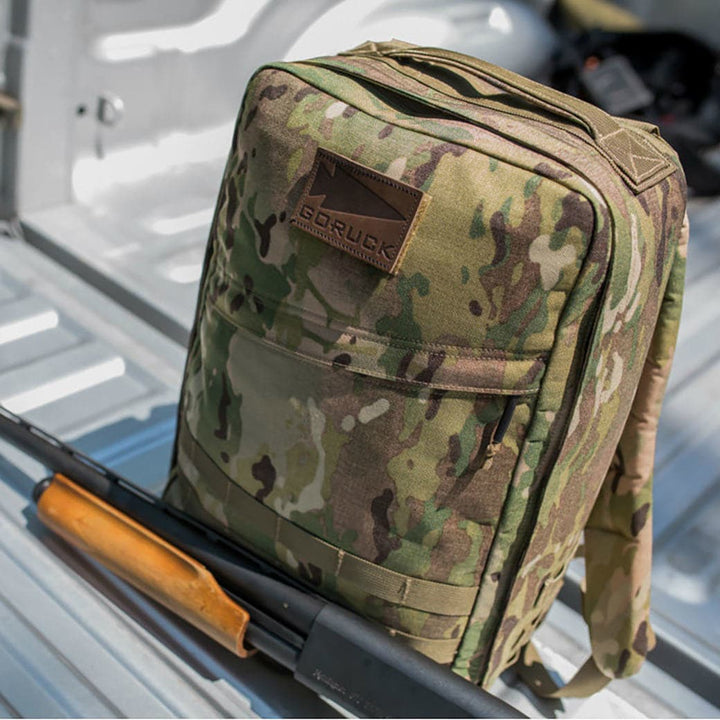 A Patch - Leather GORUCK Spearhead backpack sits on the truck bed, its rugged design enhanced by a wooden-handled tool. With genuine leather accents and a durable VELCRO® hook for easy access, this vendor-unknown backpack is crafted for adventure.