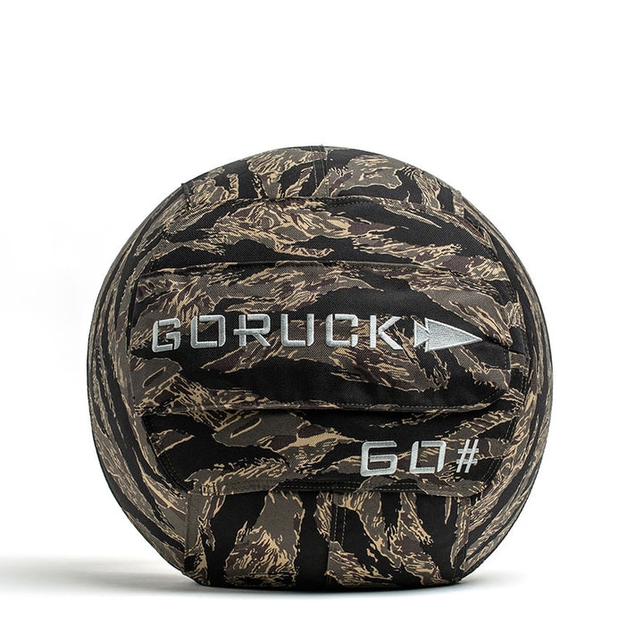 The GORUCK Sand Medicine Ball, featuring a camouflage pattern and white "GORUCK" lettering along with a "60#" marking, is perfect for improving core stability. This versatile equipment enhances any home gym by providing the benefits of traditional sand medicine balls for functional strength training.