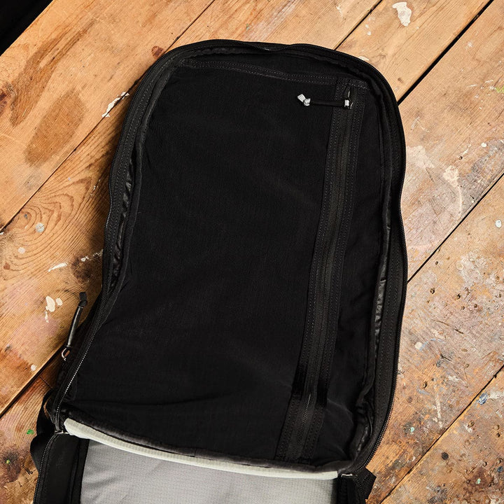 The Bullet Ruck Double Compartment by GORUCK, made from Ripstop Nylon, is displayed open on a wooden floor, highlighting its lightweight design with dual compartments and zippers.