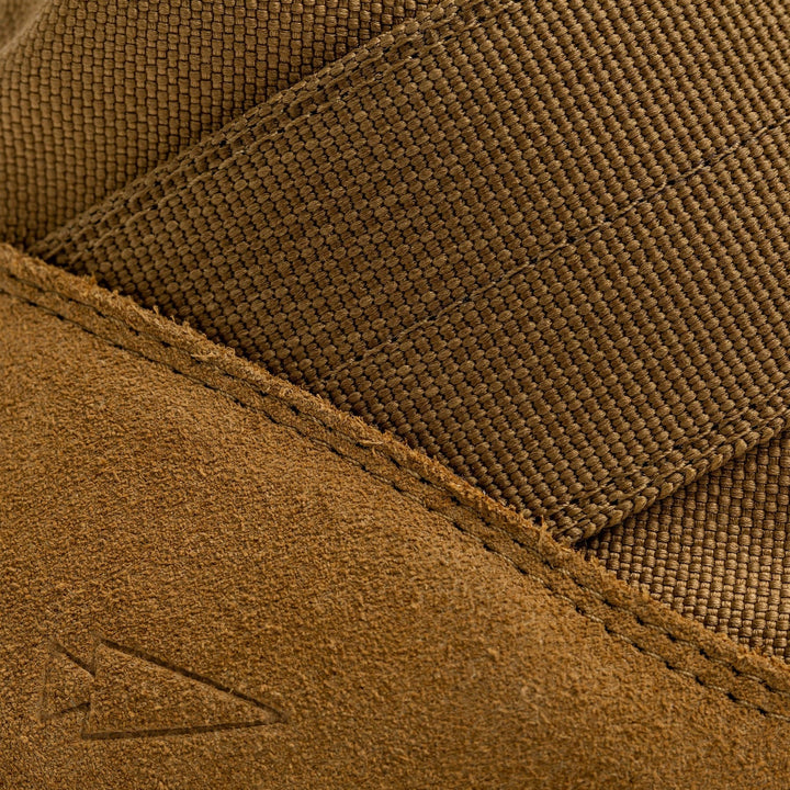 Close-up of the MACV-2 - Mid Top - Coyote by GORUCK, showcasing brown textured fabric and suede material with a small embossed arrow symbol on the bottom left, reminiscent of jungle boot design. The image highlights the contrast between the smooth and rough surfaces.