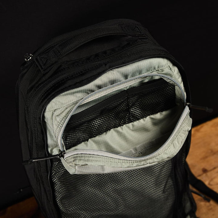 The Bullet Ruck Double Compartment by GORUCK in ripstop nylon rests on a wooden surface against a dark background.