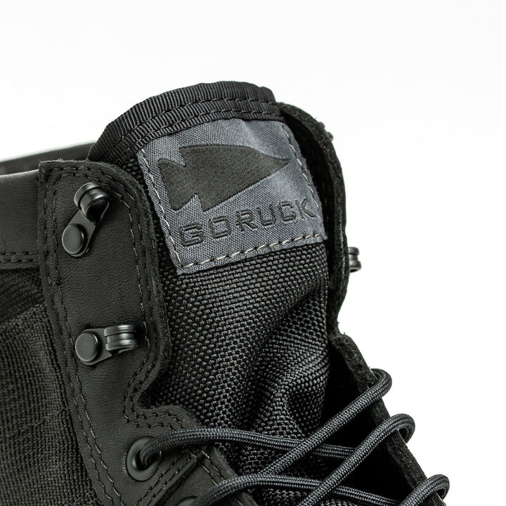 A close-up of the MACV-2 - Mid Top - Black boot showcases its rugged design, featuring sturdy eyelets and black laces. The textured fabric tongue prominently displays the GORUCK logo, complemented by a durable triple compound outsole.