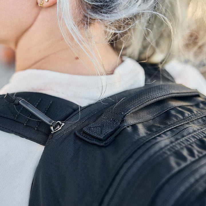 A person with white hair carries a sleek black Bullet Ruck Double Compartment - Ripstop Nylon backpack from GORUCK, featuring dual compartments for efficient storage.