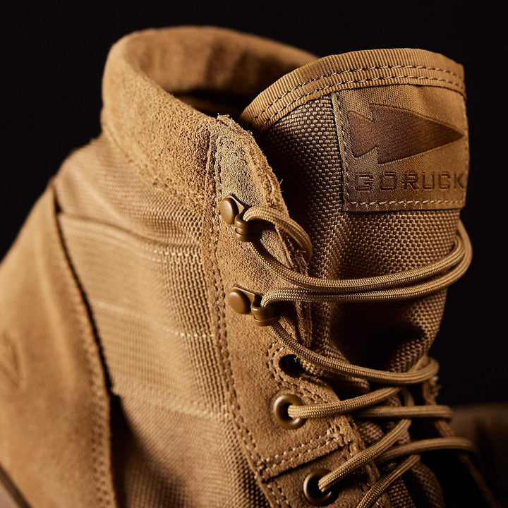 Close-up of a tan MACV-1 Hi-Speed - Mid Top boot by GORUCK, showcasing laces and a fabric tag. It features a lightweight EVA midsole against a dark background.