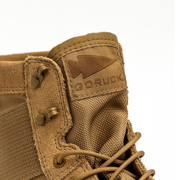 Close-up of a coyote-colored MACV-2 mid-top jungle boot featuring GORUCK's logo, which includes an arrowhead on the tongue. The design showcases sturdy lace eyelets, prominent stitching, and a triple compound outsole, emphasizing its rugged durability.