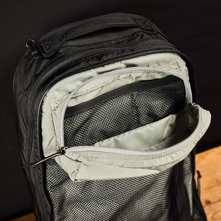 Place the GORUCK Bullet Ruck Double Compartment, made of ripstop nylon, open on a wooden surface to reveal its dual mesh compartments.