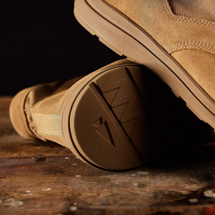 Close-up of MACV-1 Hi-Speed - Mid Top boots by GORUCK, featuring tan suede with detailed stitching, textured soles, and a lightweight EVA midsole, resting on a rustic wooden surface.