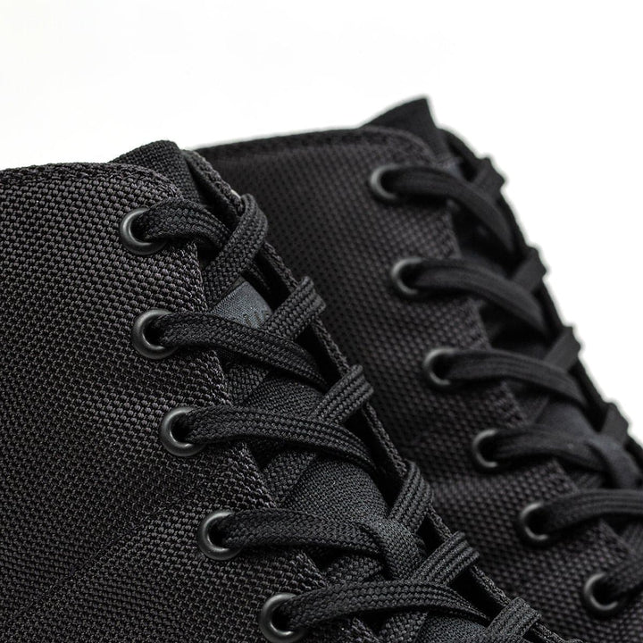 Close-up of black Ballistic Trainers - Mid Top sneakers by GORUCK, crafted with CORDURA® Ballistic Nylon and featuring black laces on a plain background. Perfect as functional fitness footwear, they offer 3X Support™ for those who demand durability and superior performance in every step.