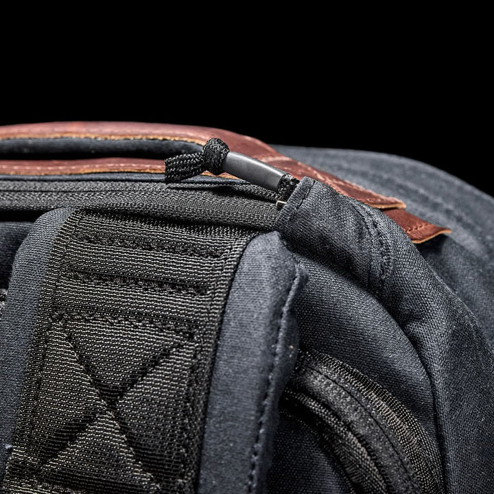 A close-up of the GR1 USA - Heritage by GORUCK showcases a waxed canvas black rucksack accented with brown leather and intricate stitching against a black background.