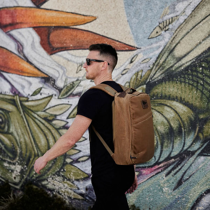 A man in sunglasses walks past a colorful mural, wearing a black t-shirt and the GORUCK GR1 USA - Heritage rucksack, perfectly complementing his style.