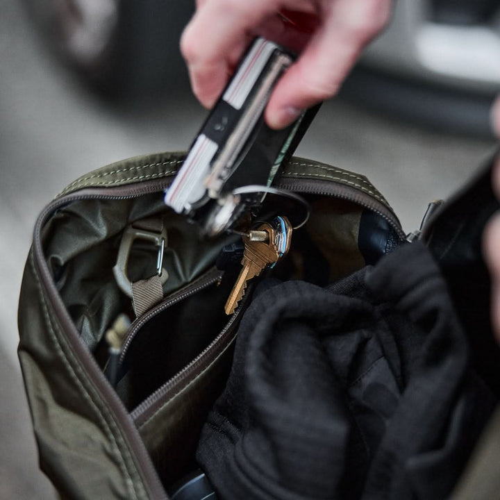 A hand reaches into an open Packable Bullet Ruck - Ripstop ROBIC® bag, holding a multitool with keys and neatly packed clothes inside.