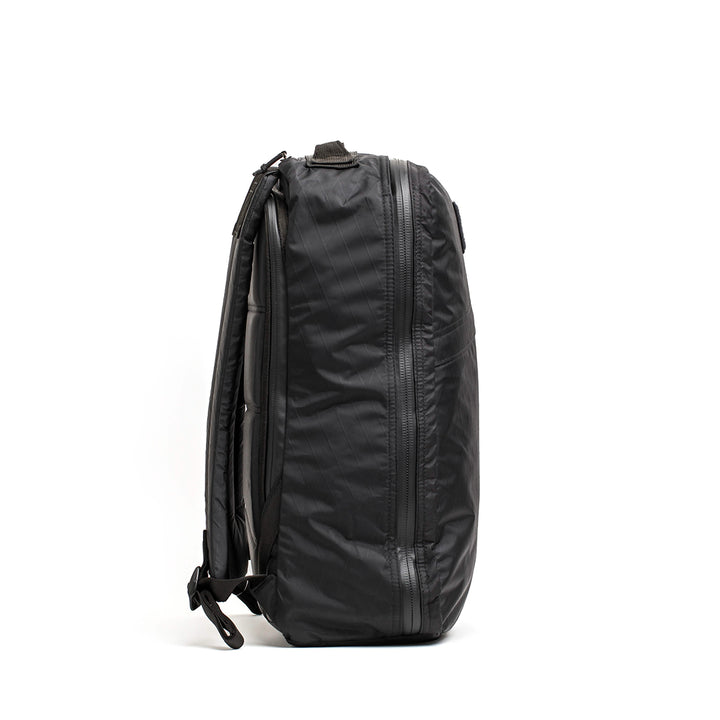 The GR1 USA - X-PAC by GORUCK is showcased from the side, highlighting its sleek black design with AquaGuard zippers, padded shoulder straps, and a handle.