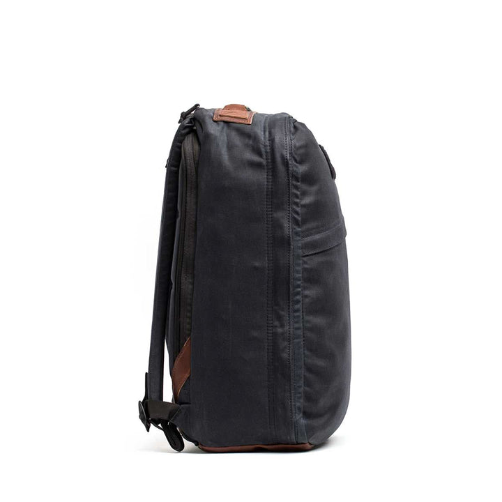 Side view of a dark gray GR1 USA - Heritage backpack by GORUCK, featuring brown leather accents and shoulder straps, made from durable waxed canvas.