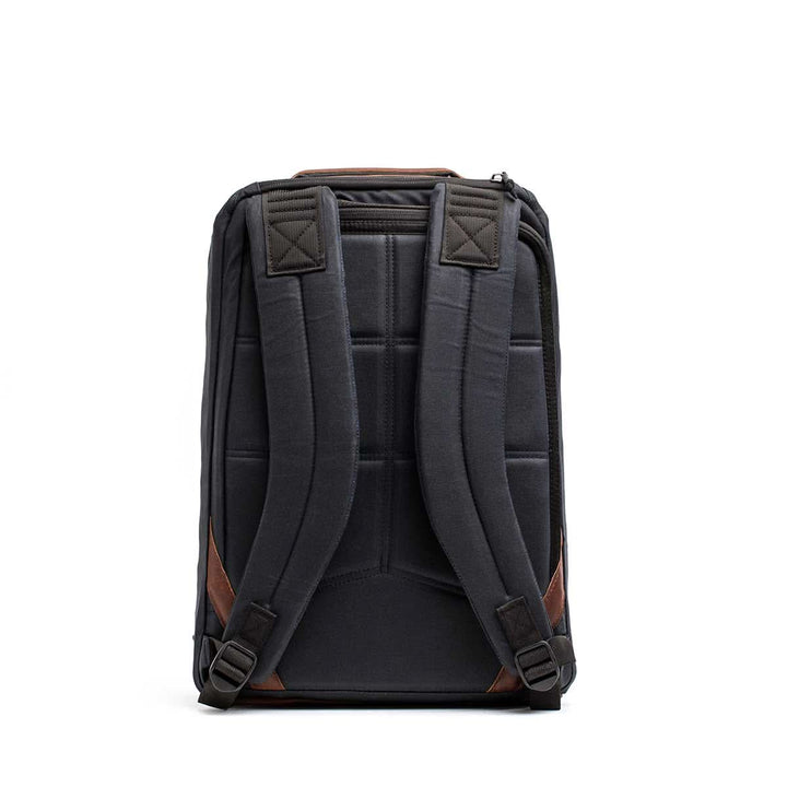 A back view of the GORUCK GR1 USA - Heritage backpack in black, made from durable waxed canvas, with padded shoulder straps and brown accents.