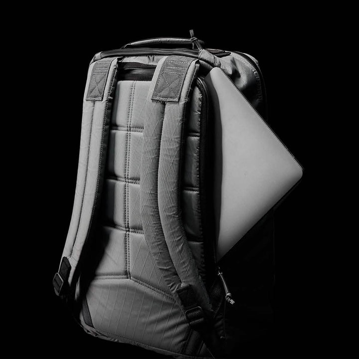 A GR1 USA - X-PAC gray backpack by GORUCK, equipped with AquaGuard zippers and a laptop partially visible in the side pocket, is set against a black backdrop.