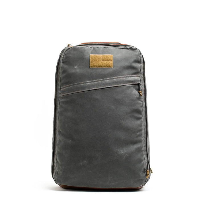 The GORUCK GR1 USA - Heritage backpack, made of waxed canvas, features a front pocket with brown accents and is topped with a unique rectangular patch.