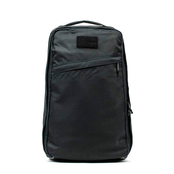 The GORUCK GR1 USA - Heritage backpack, crafted from durable waxed duck canvas, features a front zipper pocket and top handle, shown from the front in black.