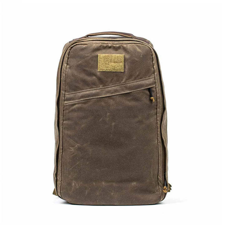 The GR1 USA - Heritage by GORUCK is a brown waxed canvas rucksack known for durability, featuring a front zipper pocket and small rectangular patch at the top.