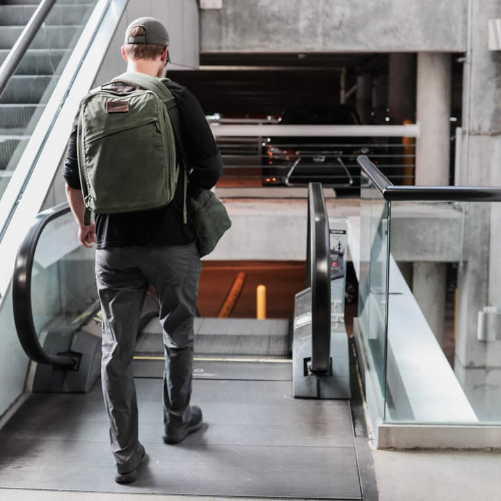 A person carrying a GR1 USA - Heritage GORUCK rucksack walks down an escalator in a parking structure.